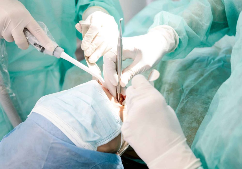 From above crop professional dentists in latex gloves using clean tools to perform oral procedure on unrecognizable patient in contemporary clinic