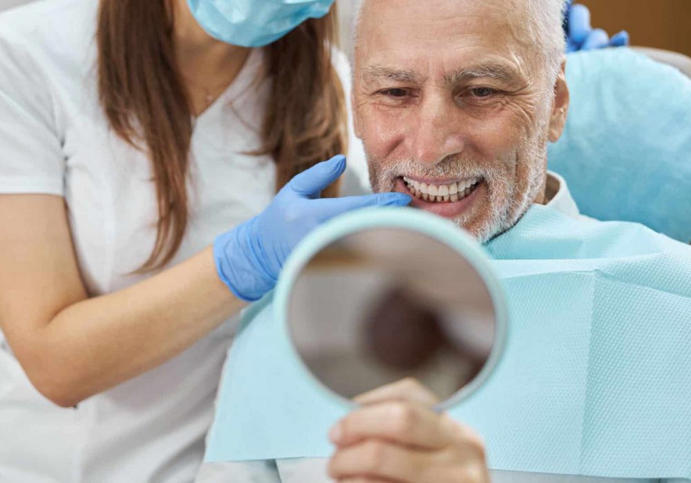 hombre mirándose al espejo para ver el resultado de sus implantes dentales